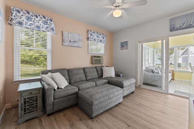 living area with light wood-type flooring, a ceiling fan, a wall unit AC, and baseboards