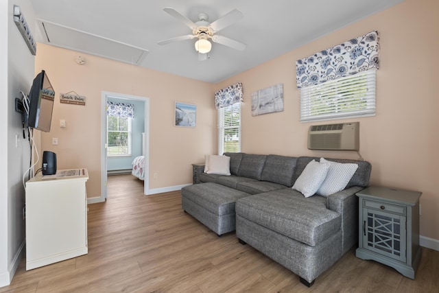 living area featuring attic access, a ceiling fan, a wall unit AC, and light wood-style floors