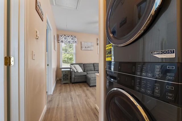 washroom featuring stacked washer and clothes dryer, baseboards, attic access, wood finished floors, and laundry area