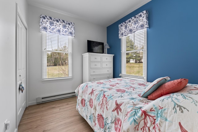 bedroom featuring baseboard heating, a closet, multiple windows, and light wood finished floors
