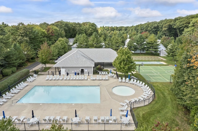 community pool with a patio, a yard, a forest view, and fence