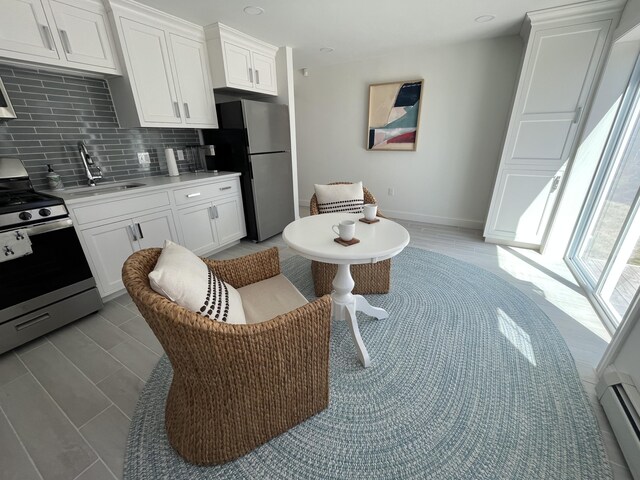 kitchen with appliances with stainless steel finishes, white cabinets, baseboard heating, and backsplash
