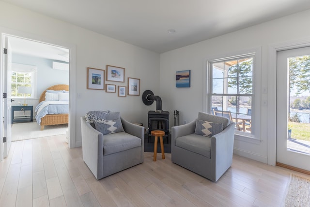 living area featuring baseboards, a healthy amount of sunlight, a wood stove, and light wood-style floors