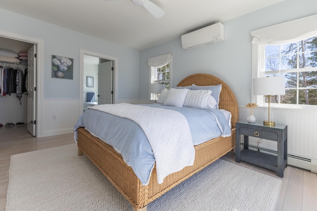 bedroom with wainscoting, a walk in closet, an AC wall unit, wood finished floors, and a closet