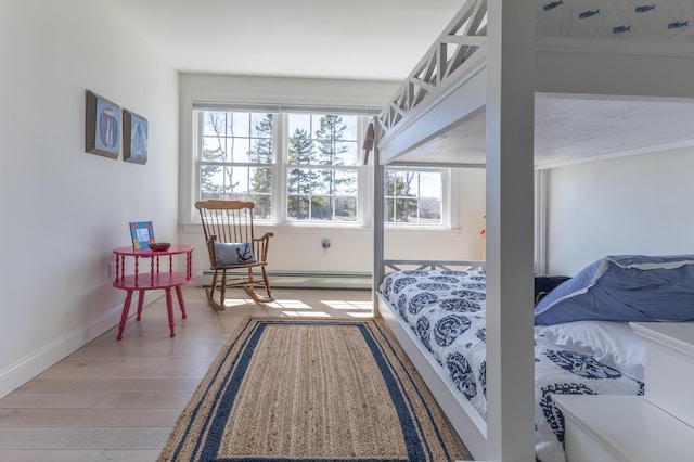 bedroom with baseboards, a baseboard heating unit, and light wood-style flooring