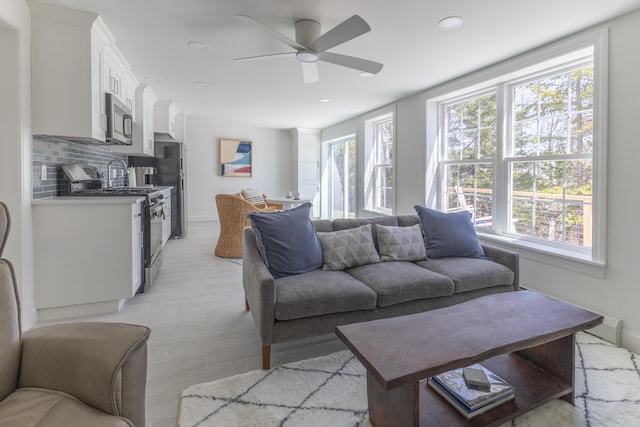 living area featuring a ceiling fan, baseboards, recessed lighting, and light wood-style floors