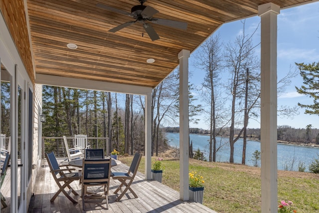 wooden terrace featuring outdoor dining area, a water view, a ceiling fan, and a lawn