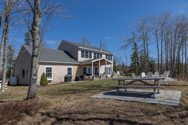 rear view of property with a lawn, roof with shingles, and a patio area