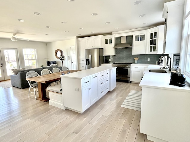 kitchen with wall chimney range hood, appliances with stainless steel finishes, a sink, tasteful backsplash, and a kitchen island