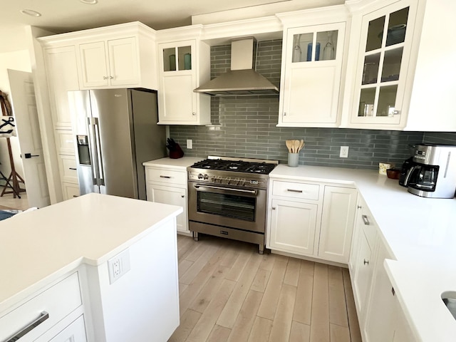 kitchen with decorative backsplash, light wood-type flooring, light countertops, stainless steel appliances, and wall chimney exhaust hood