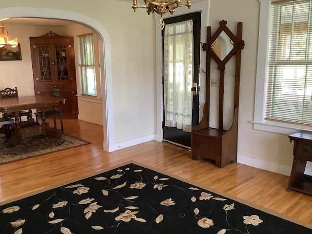 foyer entrance featuring arched walkways, wood finished floors, a healthy amount of sunlight, and a notable chandelier