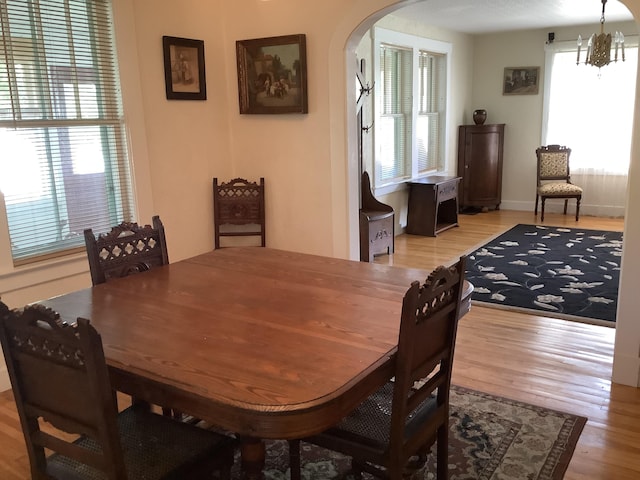 dining space featuring a notable chandelier, arched walkways, light wood-style floors, and a healthy amount of sunlight