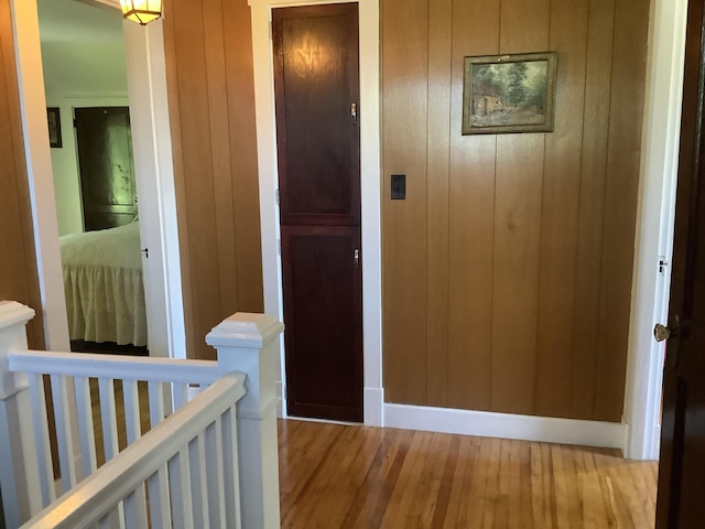 corridor with wood walls, an upstairs landing, light wood finished floors, and baseboards
