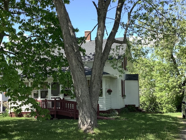 view of home's exterior featuring a lawn, a shingled roof, a chimney, and a deck
