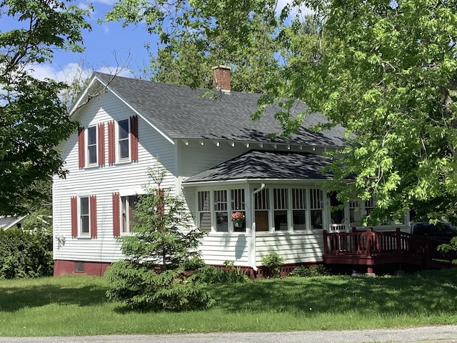 exterior space featuring a chimney, a wooden deck, a shingled roof, and a lawn