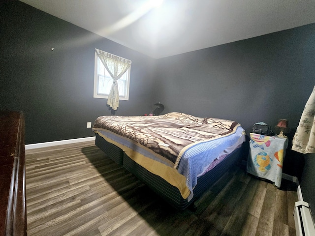 bedroom with a baseboard heating unit, baseboards, lofted ceiling, and wood finished floors