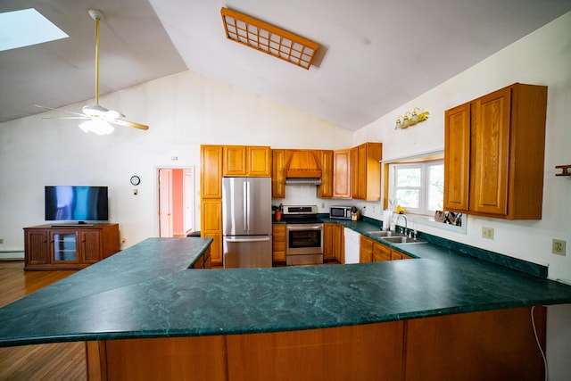 kitchen with dark countertops, appliances with stainless steel finishes, a sink, brown cabinetry, and wood finished floors