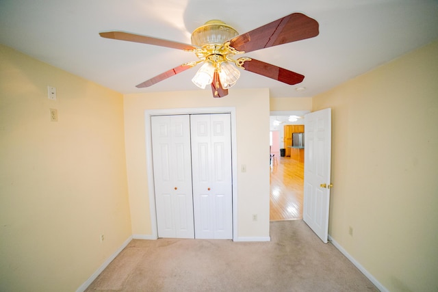unfurnished bedroom featuring a closet, freestanding refrigerator, light carpet, baseboards, and a ceiling fan