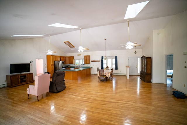 living room with baseboard heating, high vaulted ceiling, a ceiling fan, light wood-style flooring, and a skylight