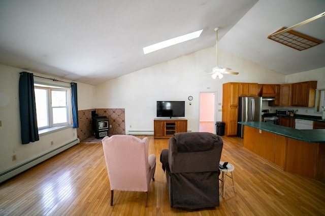 living room featuring a skylight, baseboard heating, a wood stove, a baseboard radiator, and light wood-style floors