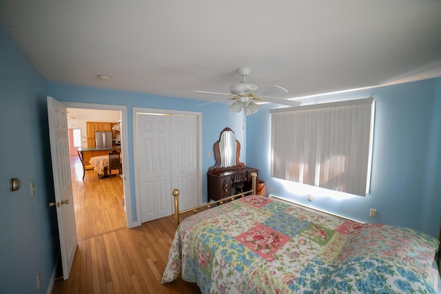 bedroom featuring a closet, freestanding refrigerator, wood finished floors, baseboard heating, and a ceiling fan