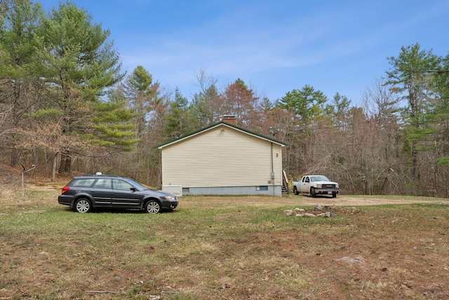 view of side of home featuring a lawn, a view of trees, a chimney, and crawl space