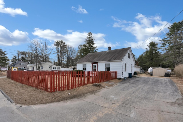 99 Ocean Park Rd, Saco, ME 04072 - view of side of property featuring a fenced front yard, a chimney, driveway, an outdoor structure, and a storage unit