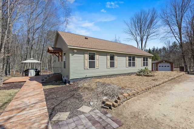 view of front of property featuring an outdoor structure, roof with shingles, and a garage