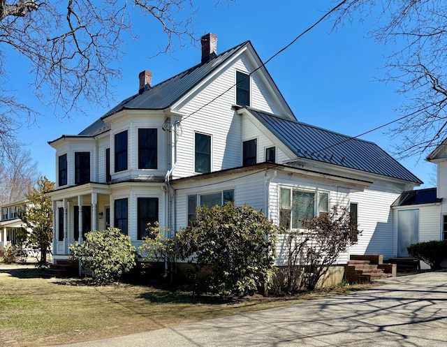 view of property exterior with a standing seam roof, a chimney, entry steps, and metal roof