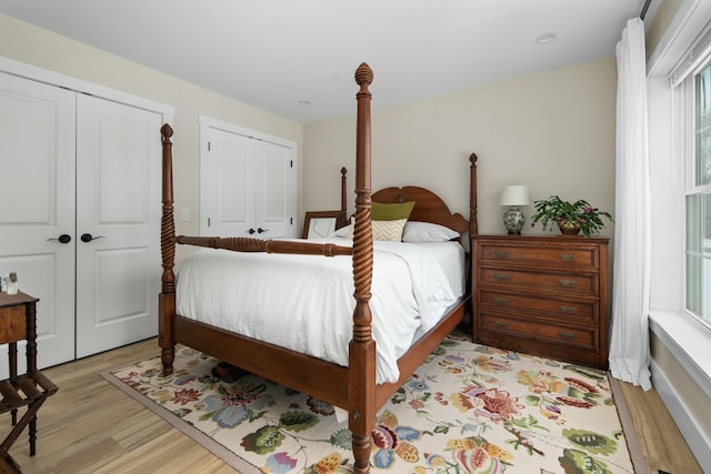 bedroom with light wood-style flooring, two closets, and multiple windows
