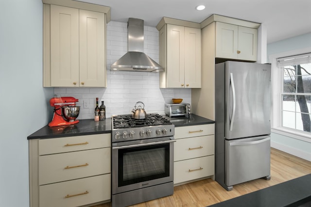 kitchen with wall chimney exhaust hood, stainless steel appliances, decorative backsplash, and dark countertops