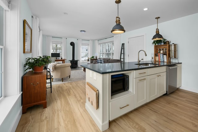 kitchen featuring stainless steel dishwasher, a sink, dark countertops, black microwave, and a wood stove