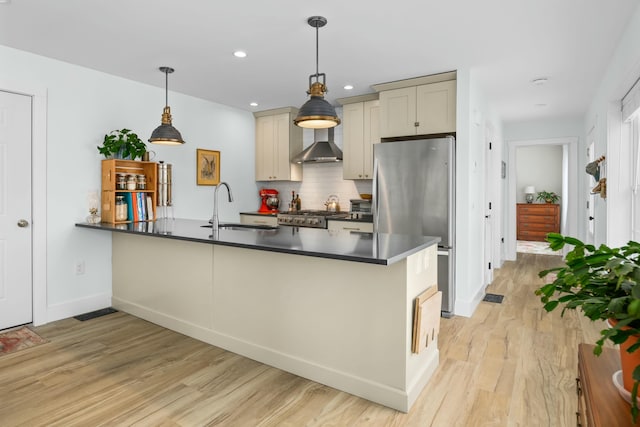 kitchen with light wood finished floors, a sink, freestanding refrigerator, wall chimney exhaust hood, and a peninsula