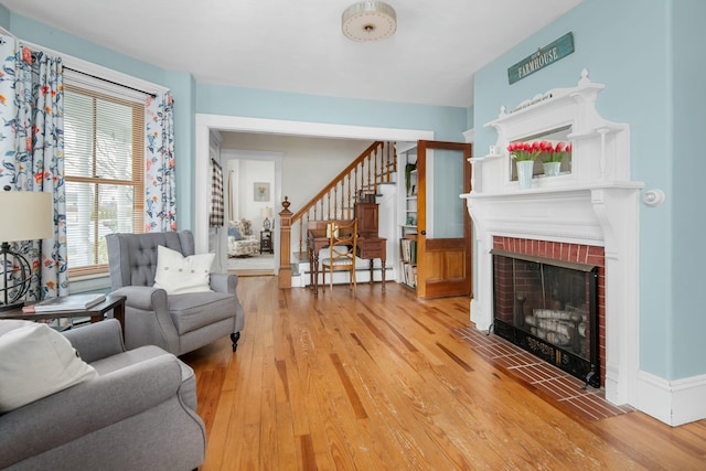 living area with a fireplace, light wood-type flooring, a baseboard heating unit, and stairway