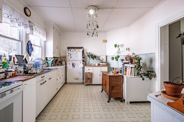 kitchen with white appliances, white cabinets, ornamental molding, and light floors