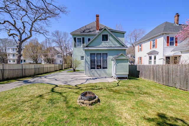 back of property with a chimney, a lawn, a patio area, a fenced backyard, and an outdoor fire pit