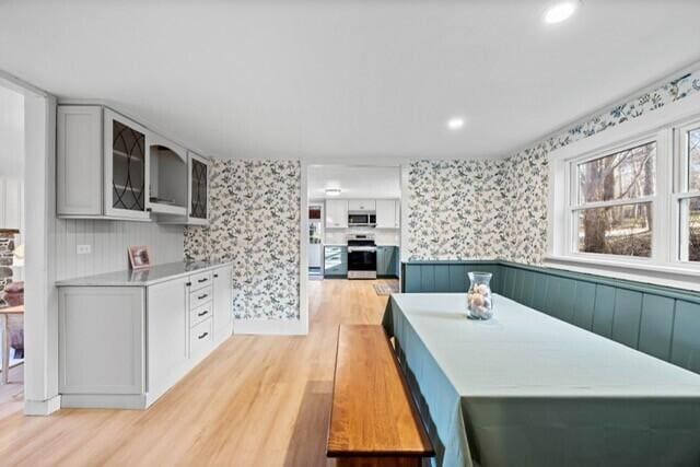 5 Paddy Creek Rd Unit 5, Kennebunkport, ME 04046 - kitchen with stainless steel appliances, wallpapered walls, light wood-type flooring, a wainscoted wall, and glass insert cabinets