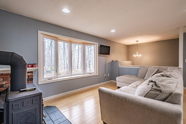 living area featuring baseboards, a notable chandelier, a wood stove, and light wood-style floors