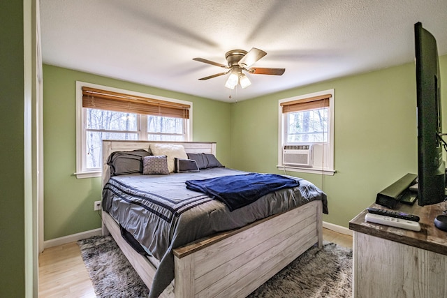 bedroom featuring baseboards, light wood-type flooring, a textured ceiling, cooling unit, and a ceiling fan