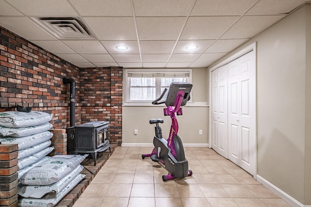 exercise room featuring visible vents, a wood stove, light tile patterned flooring, baseboards, and a drop ceiling