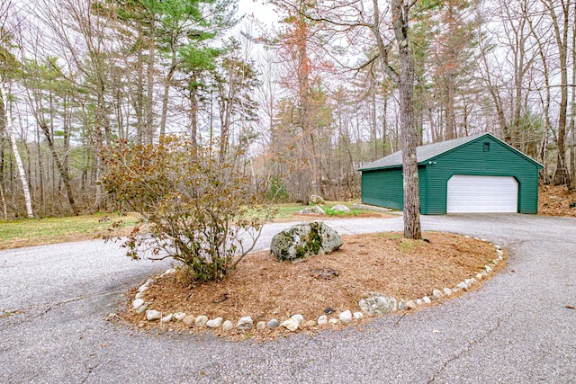 view of property exterior with a detached garage, curved driveway, and an outbuilding