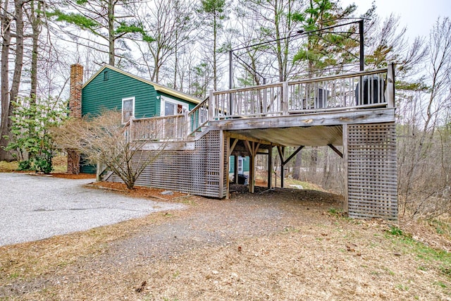 exterior space featuring a chimney, dirt driveway, a wooden deck, a carport, and stairway