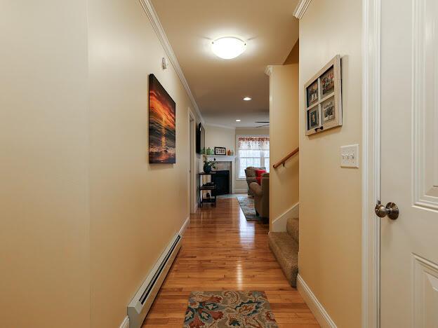14 Connor Dr Unit 14, Gorham, ME 04038 - hallway featuring crown molding, baseboard heating, light wood-style flooring, baseboards, and stairway