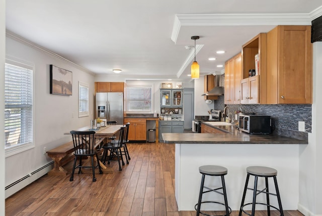kitchen featuring a peninsula, appliances with stainless steel finishes, baseboard heating, a sink, and wall chimney exhaust hood