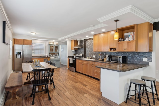 kitchen featuring wall chimney range hood, decorative backsplash, appliances with stainless steel finishes, dark countertops, and a peninsula