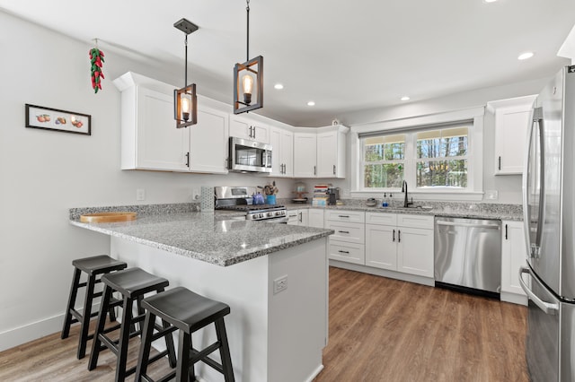 31 Neptune Dr, Brunswick, ME 04011 - kitchen with a peninsula, white cabinetry, light stone counters, a sink, and appliances with stainless steel finishes