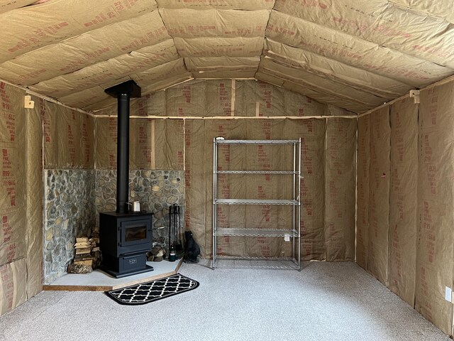 unfurnished living room with carpet floors, a wood stove, and lofted ceiling