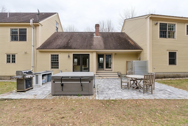 rear view of property featuring a hot tub, a lawn, a chimney, and a patio area