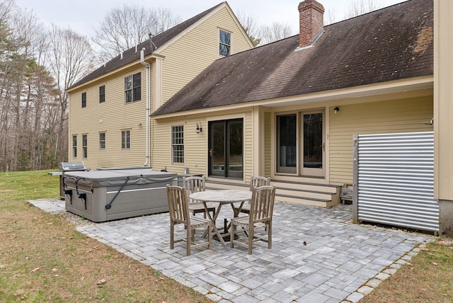 back of property with roof with shingles, a chimney, a patio area, a lawn, and a hot tub