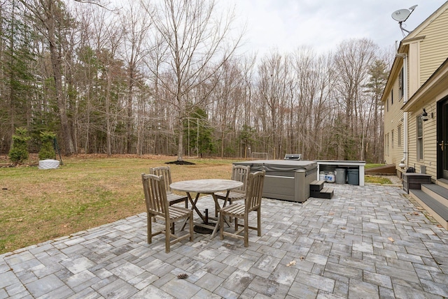 view of patio / terrace with a hot tub, a view of trees, and outdoor dining space